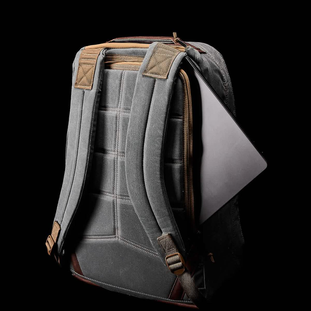 Gray GORUCK GR1 USA - Heritage Rucksack with padded straps, a partially open side pocket showing the edge of a laptop, on a black background.