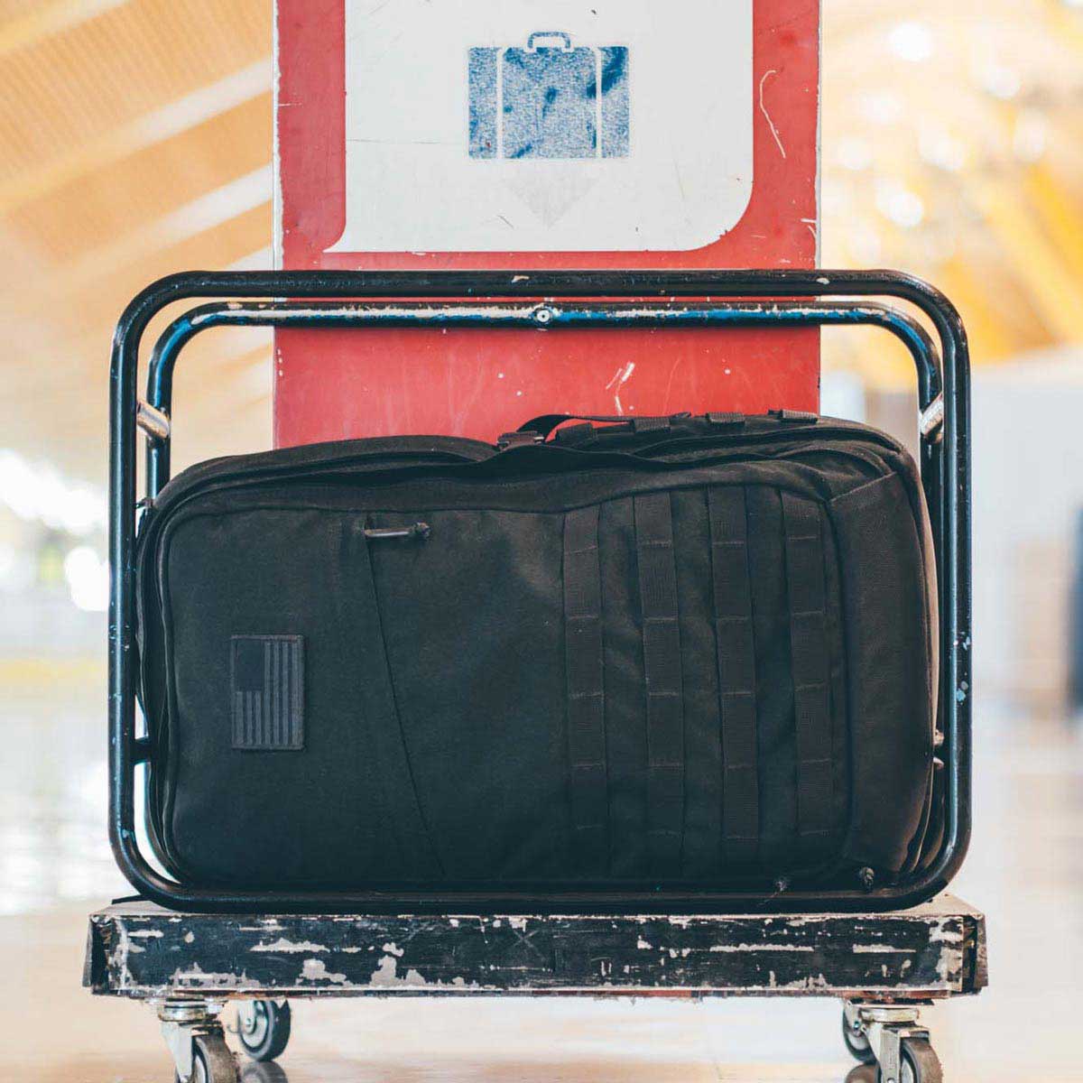A black duffel bag sits on a luggage cart in front of a luggage sign at a station.