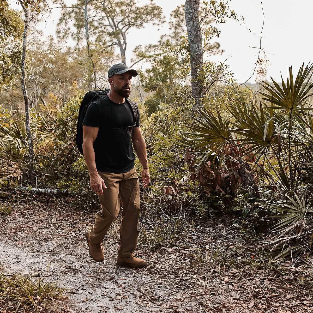 Man rucking with GORUCK backpack on forest trail, wearing outdoor gear and grey hat