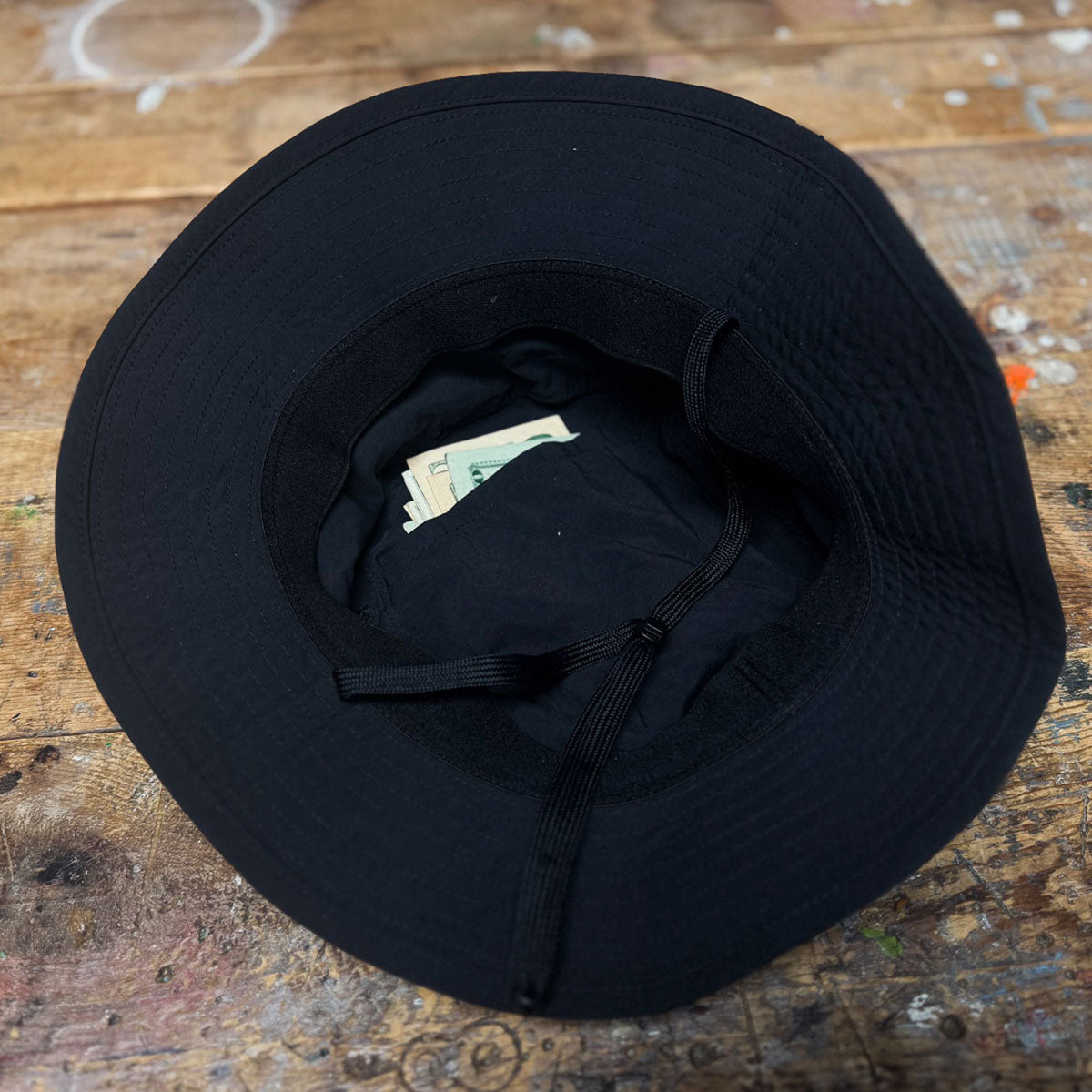 A black hat turned upside down with cash inside, sitting on a worn wooden surface.