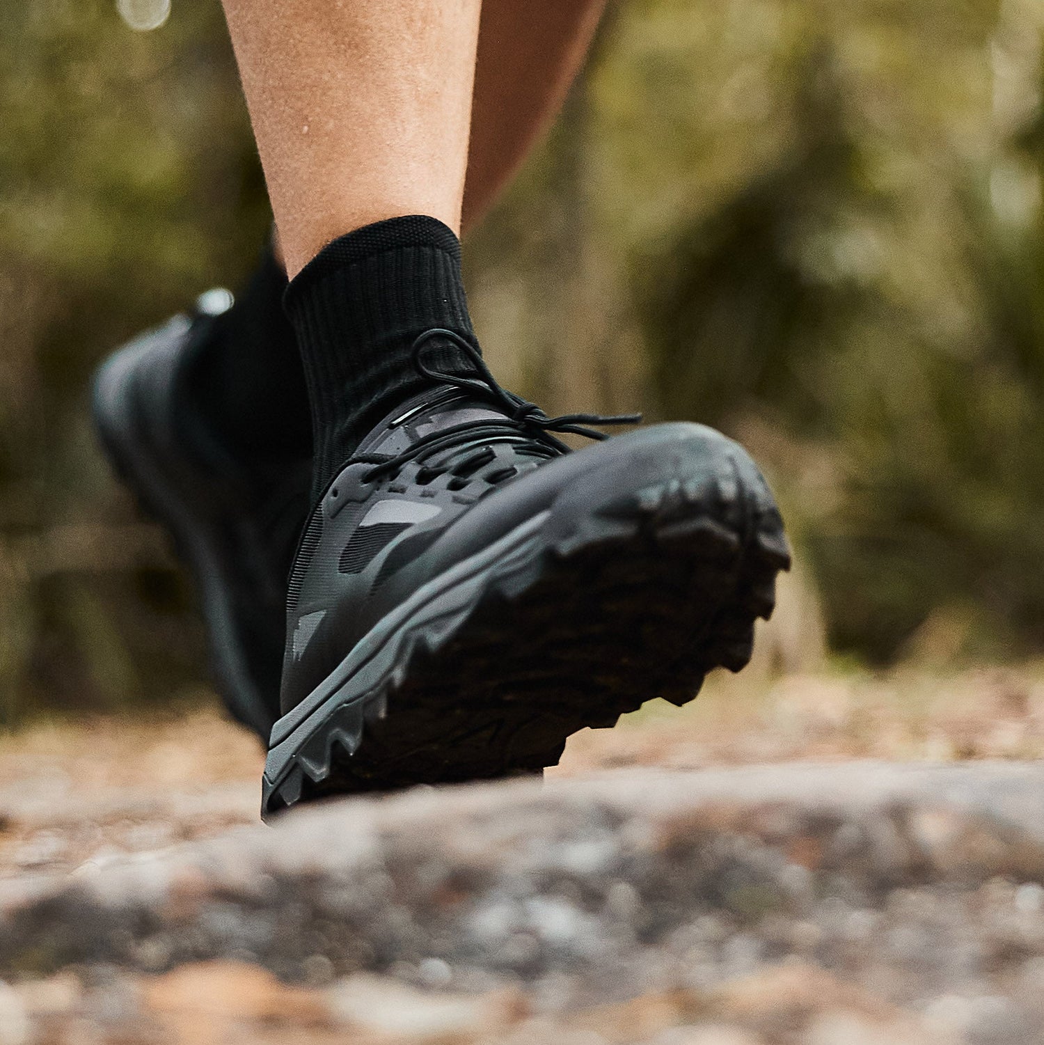 Close-up of a person wearing black trail running shoes walking on a rocky outdoor path.