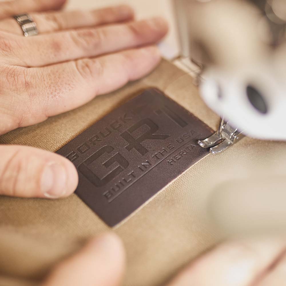 Close-up of hands sewing a GORUCK GR1 patch onto fabric with a sewing machine.