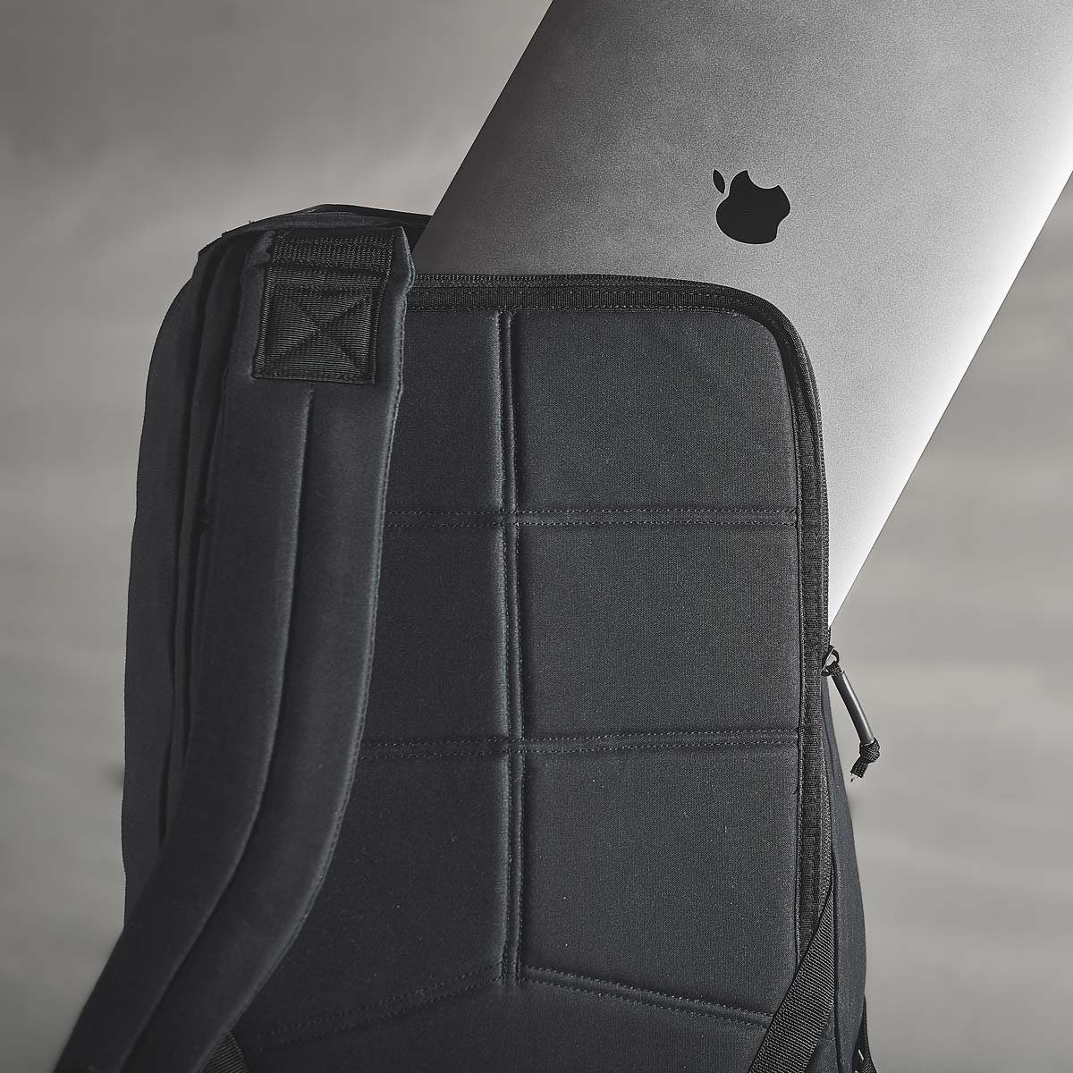 A black laptop bag with a visible Apple MacBook partially inside against a gray background.