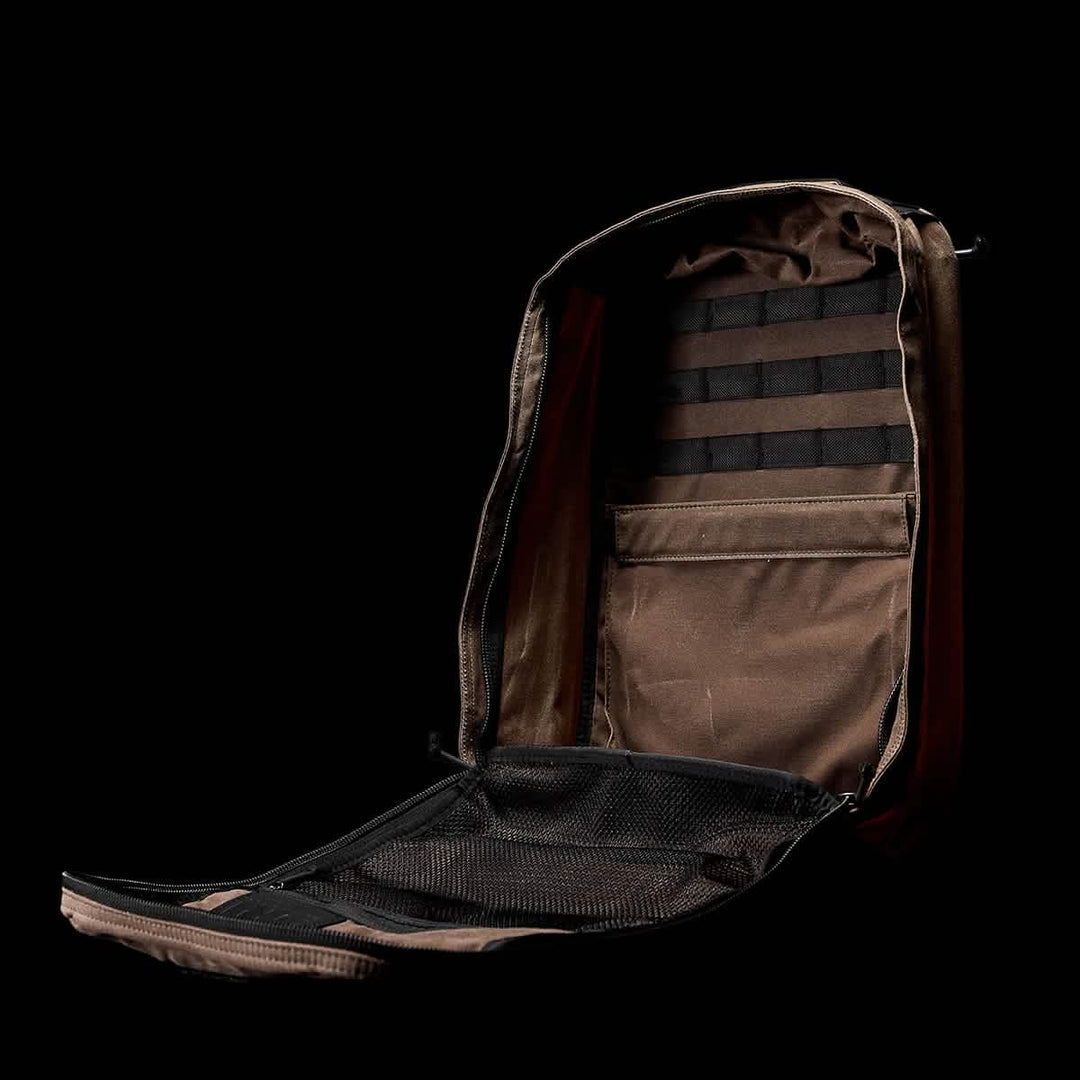 Set against a black background, the GR1 USA - Heritage by GORUCK is shown open, revealing its interior pockets and mesh compartments perfect for organization. With a bombproof laptop compartment, this brown retro canvas rucksack merges durability with timeless style.