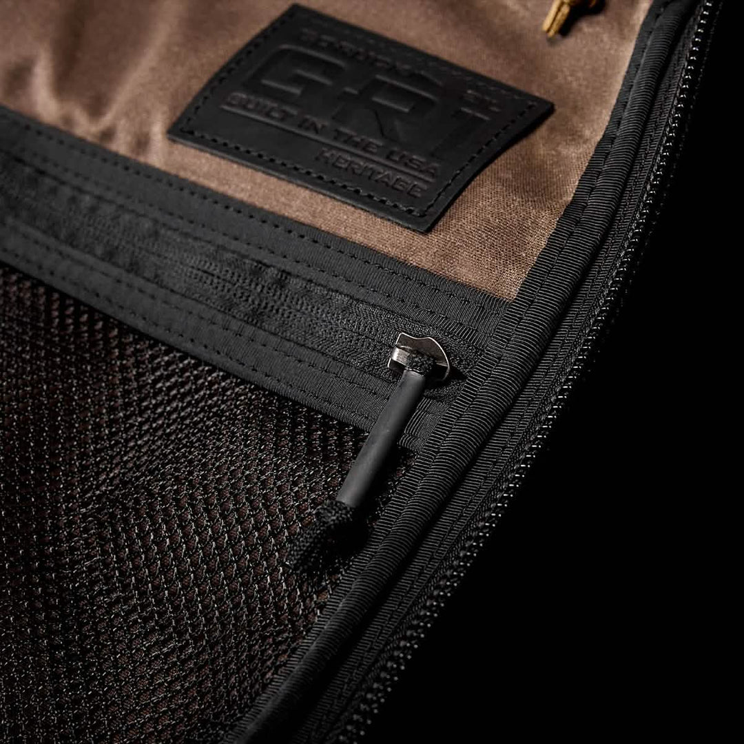 Close-up of a zippered compartment in the GORUCK GR1 USA - Heritage, showcasing a mesh pocket and a brown label stitched above the zipper, made from durable waxed duck canvas.