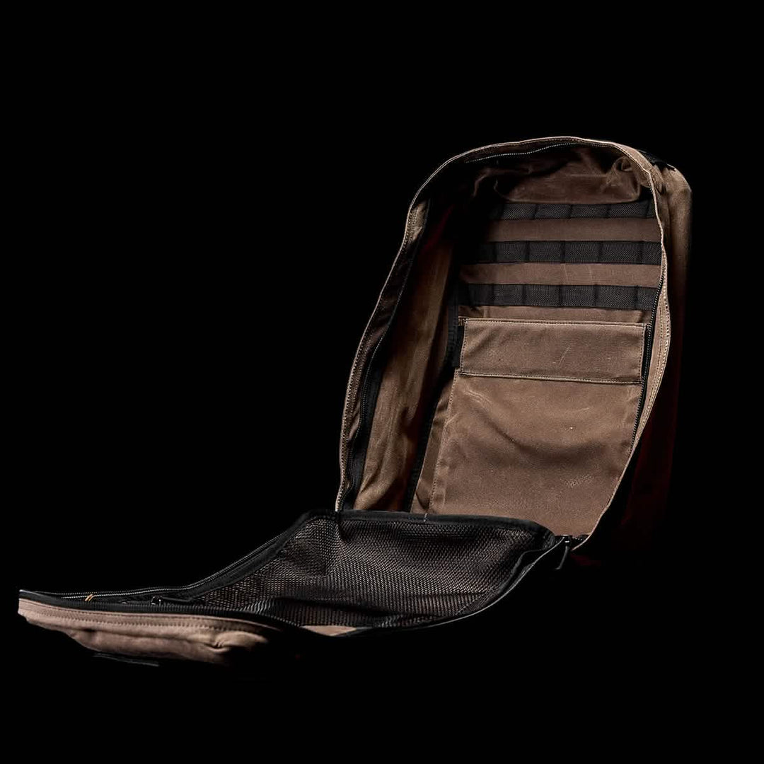 The GR1 USA - Heritage by GORUCK is an open brown backpack made from durable waxed duck canvas with multiple compartments, shown on a black background.