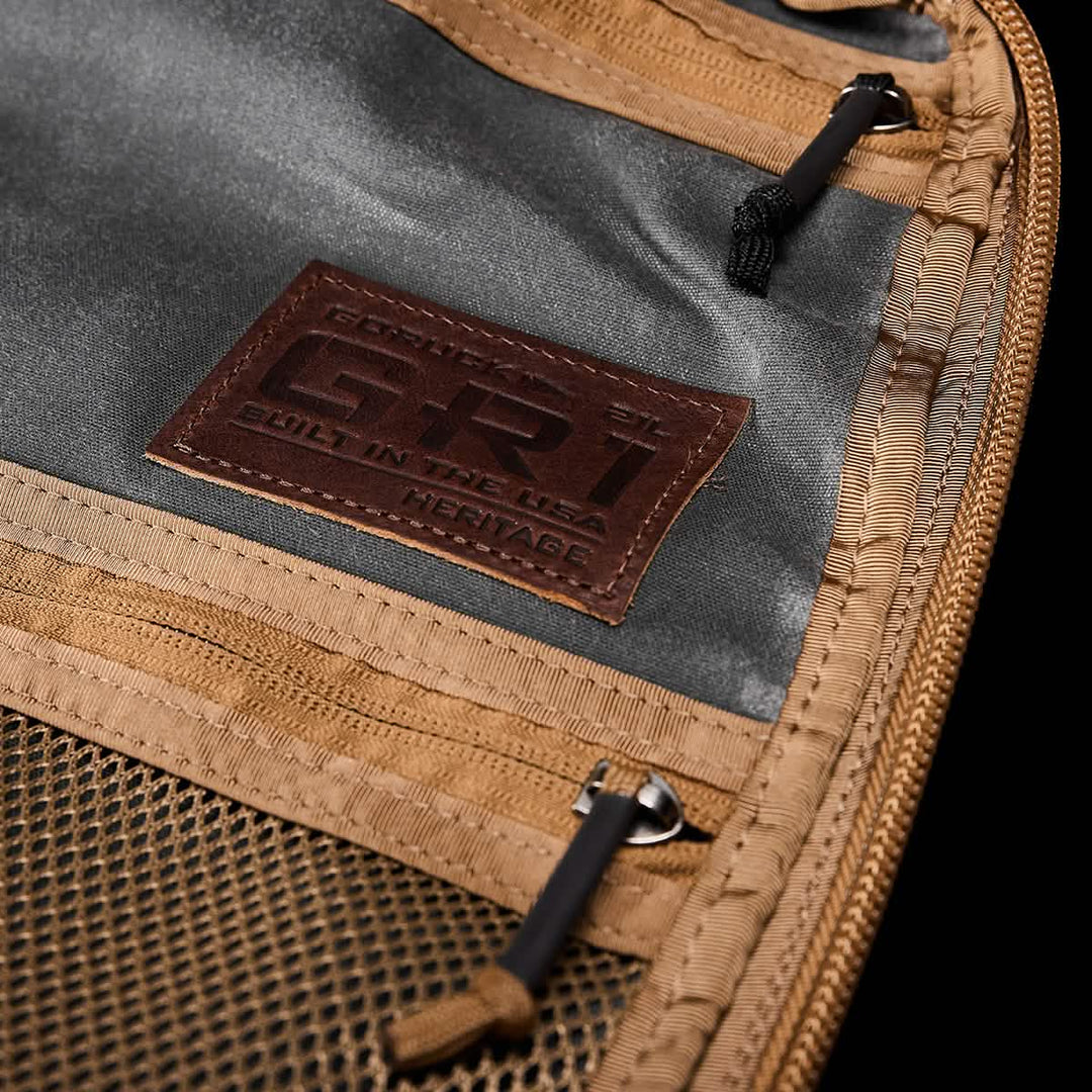 The GR1 USA - Heritage by GORUCK showcases a brown and gray waxed duck canvas interior with a zipper, mesh pocket, and leather "GR1 Built in the USA Heritage" patch, exuding the timeless appeal of a rucksack finished with Martexin Wax.