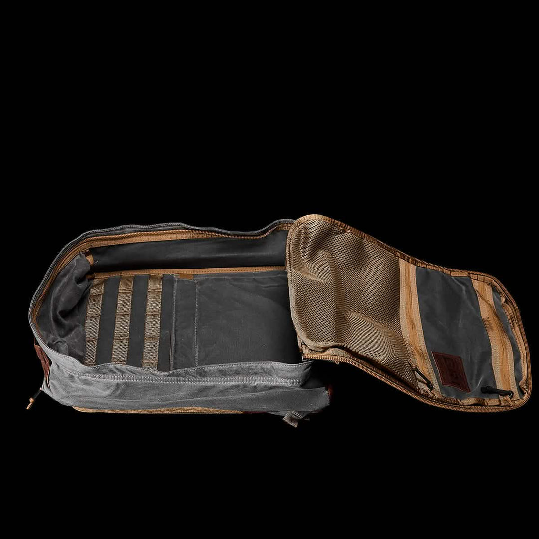 The GR1 USA - Heritage by GORUCK, crafted from durable Waxed Duck Canvas with a Martexin Wax Finish, sits open against a black background, revealing its interior compartments and mesh pocket, blending timeless style with practical functionality.
