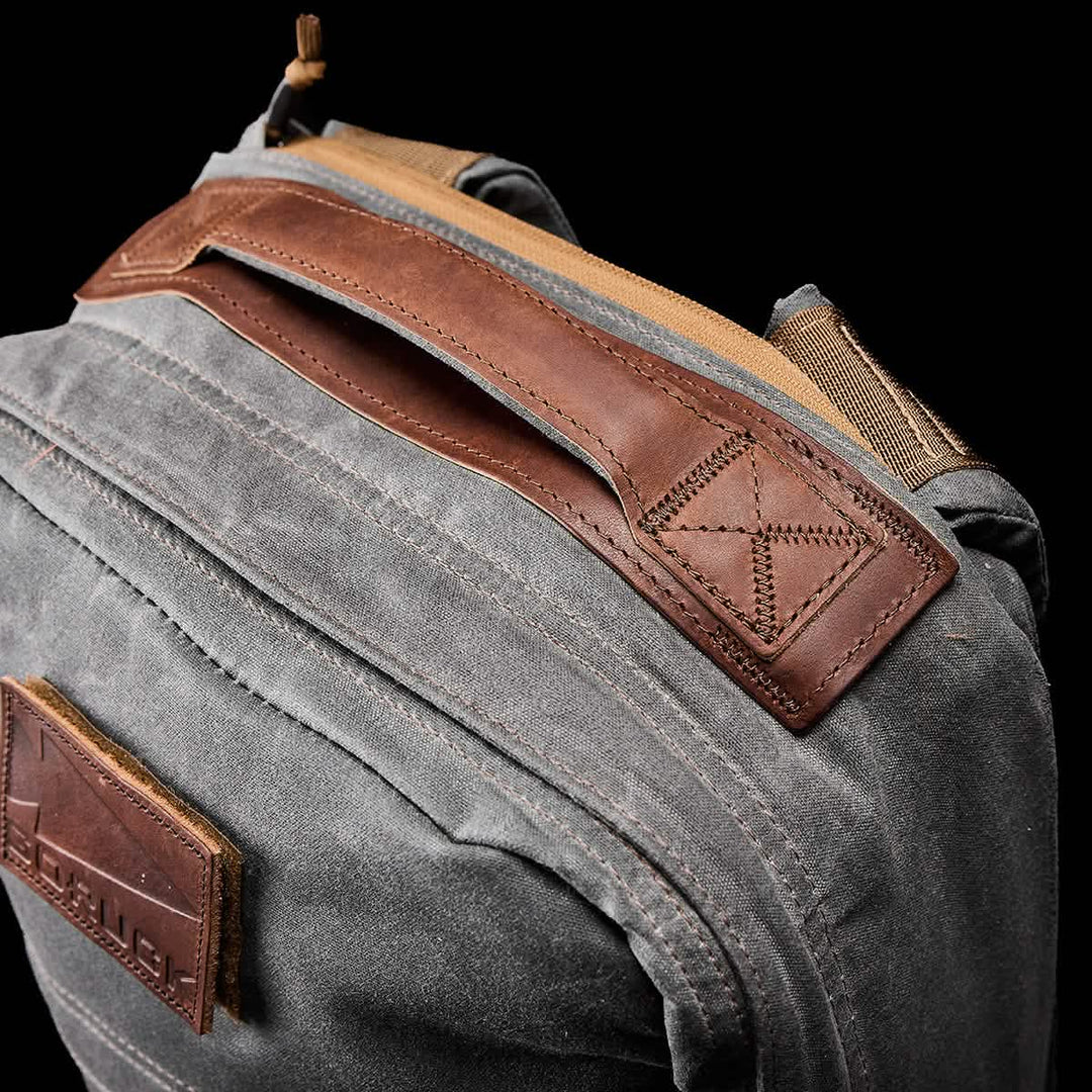 Close-up of a gray GR1 USA - Heritage rucksack by GORUCK, featuring brown leather accents on the handle and trim, crafted from durable Waxed Duck Canvas with a classic Martexin Wax Finish.