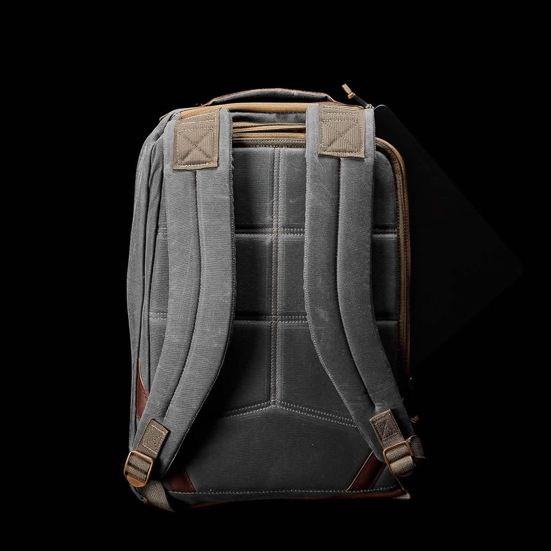 The GR1 USA - Heritage by GORUCK is a gray waxed duck canvas backpack with padded straps and brown accents, shown from the back on a black background.