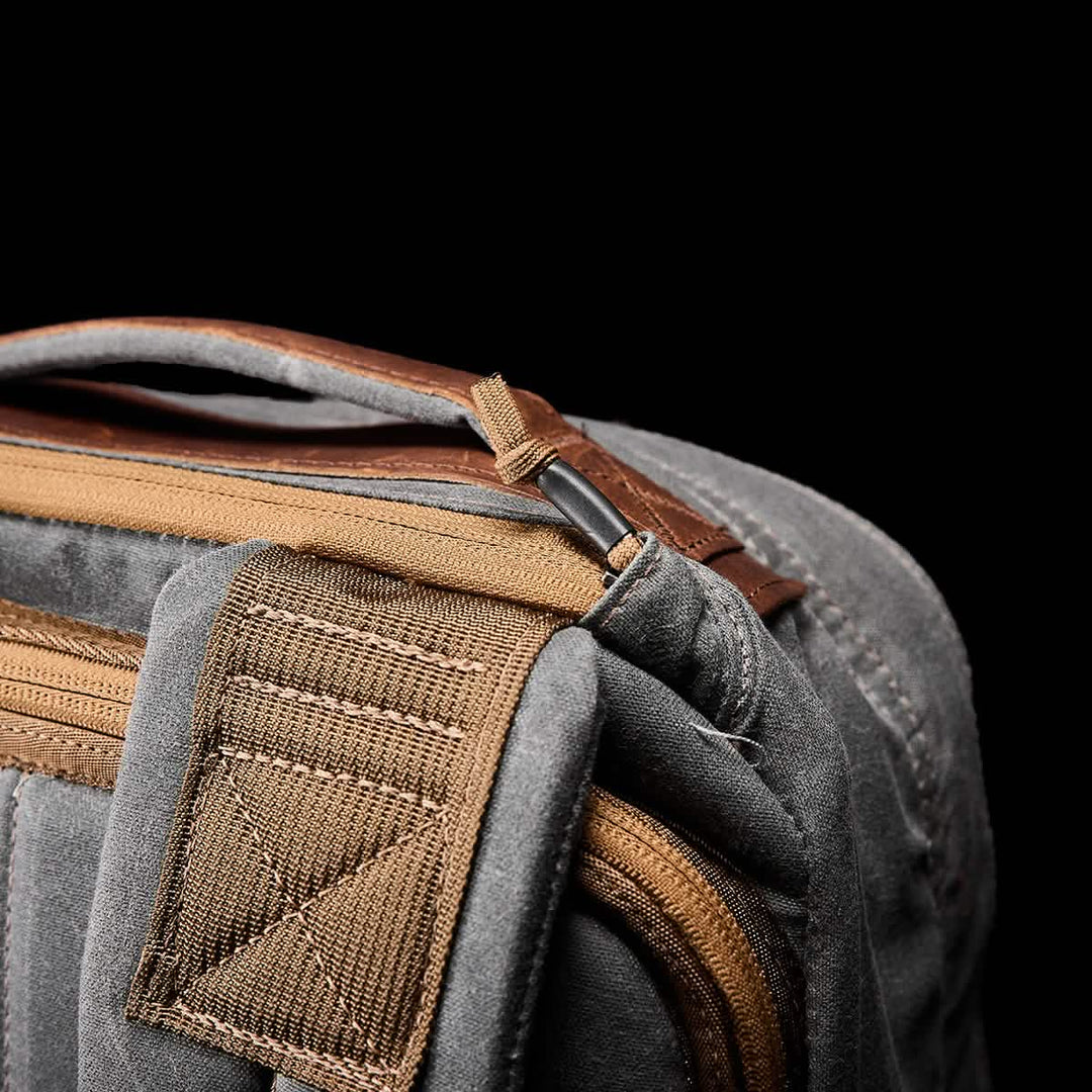Close-up of the GR1 USA - Heritage by GORUCK, a gray and tan waxed duck canvas fabric bag with a strap and zipper, set against a black background.