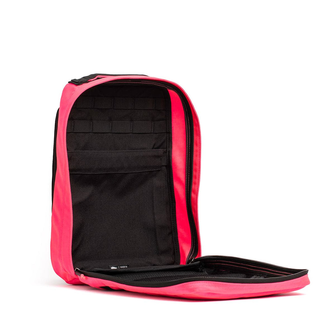 The GR0 - Cordura by GORUCK is showcased against a plain white background with its vibrant pink color. This compact backpack includes a bombproof laptop compartment and an open design that reveals a black interior with pockets, ideal for minimalist EDC organization.