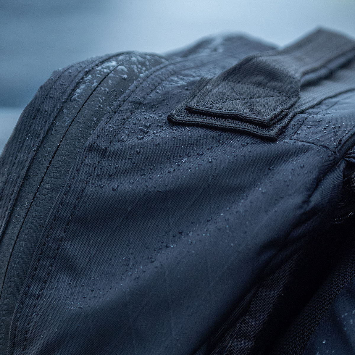Close-up of a black bag with water droplets on its surface, showing its water-resistant material.