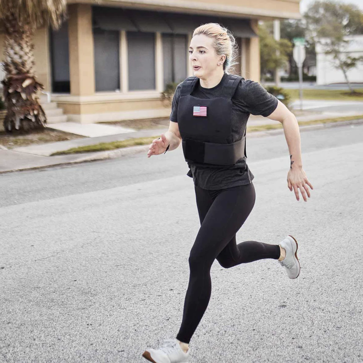 Woman running outdoors wearing athletic clothes and a weighted vest with a small American flag patch.