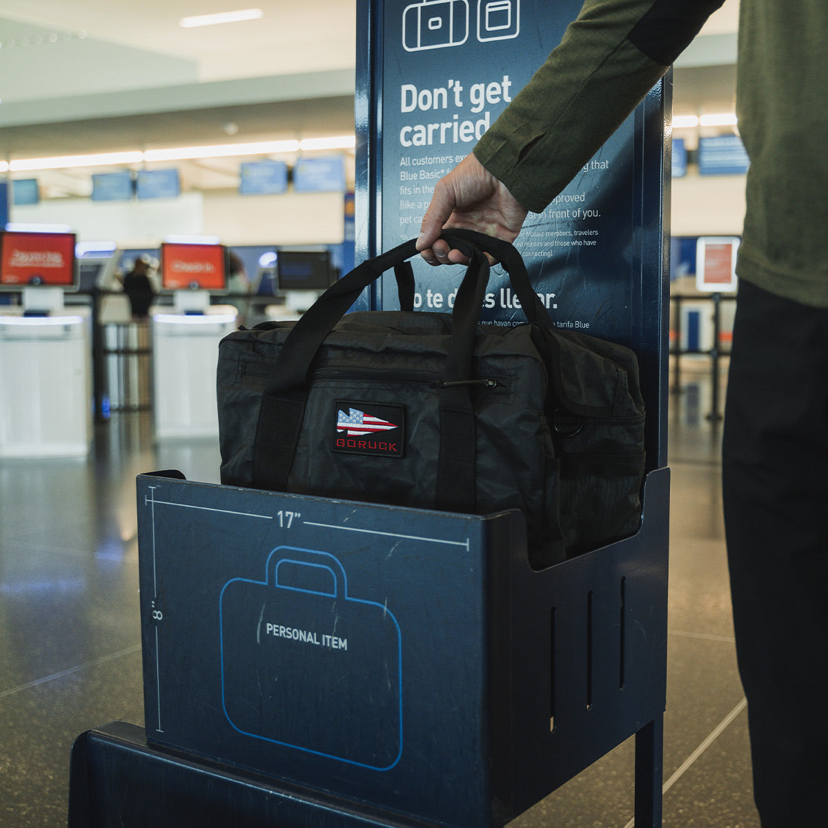 Person placing a black duffel bag into an airline personal item size checker at an airport.