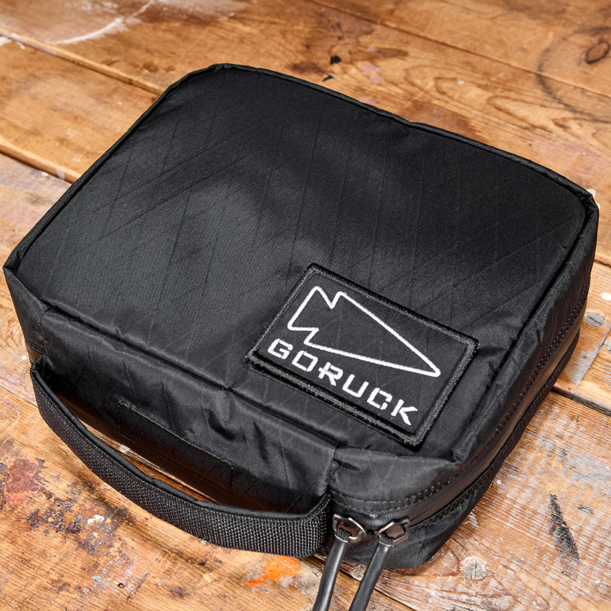 Black GORUCK pouch with logo patch on a wooden surface, showing zippers and a carrying handle.