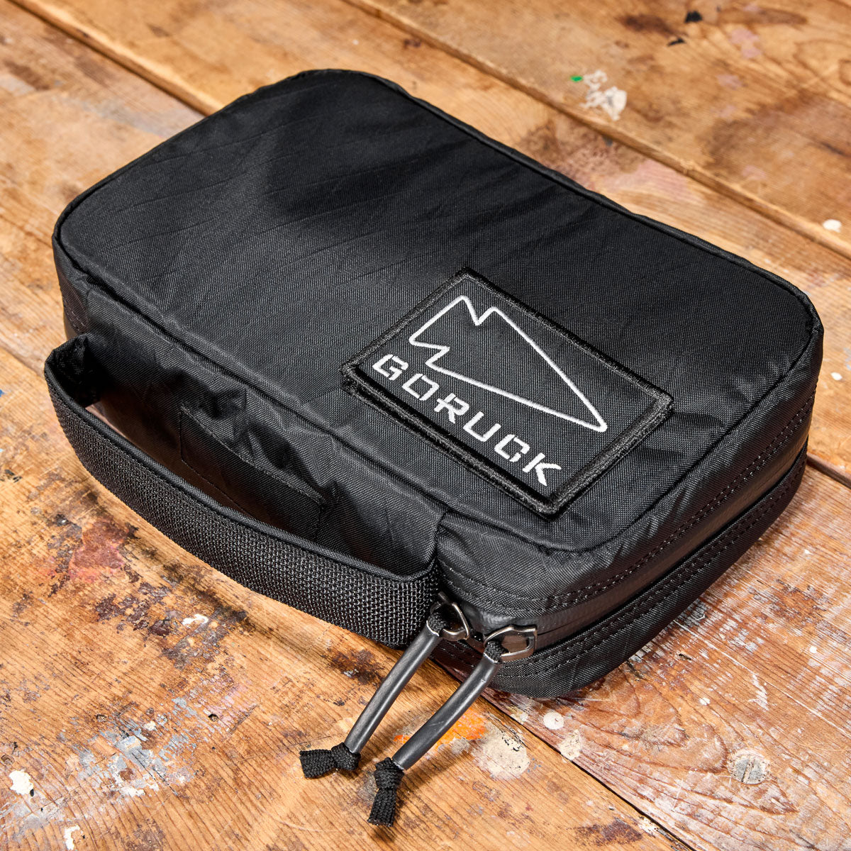 Black GORUCK pouch with zippers and handle, placed on a rustic wooden surface.