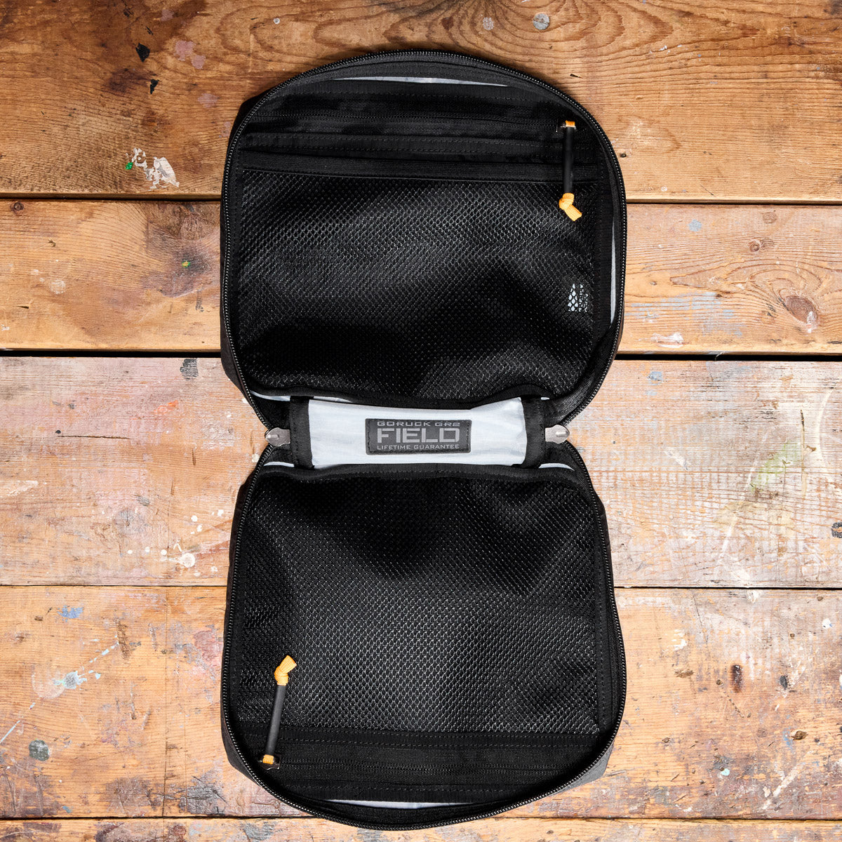 Black zippered mesh organizer pouch open on a rustic wooden surface, showing empty compartments.