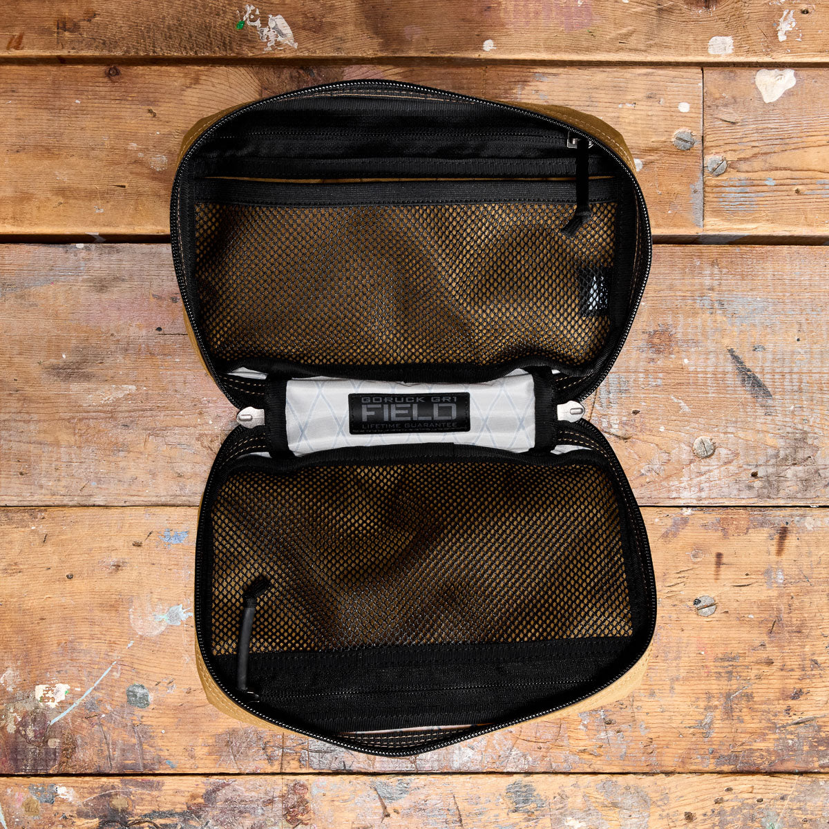 An open black and tan pouch with mesh pockets, lying on a worn wooden surface.