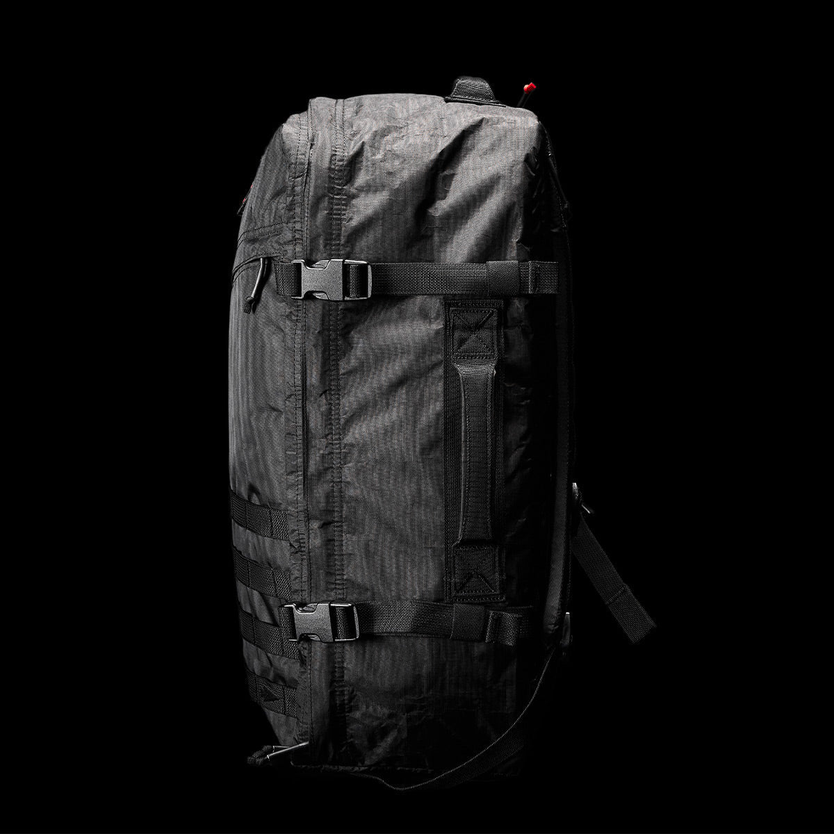 A black, rugged backpack with buckles and side handle against a black background.