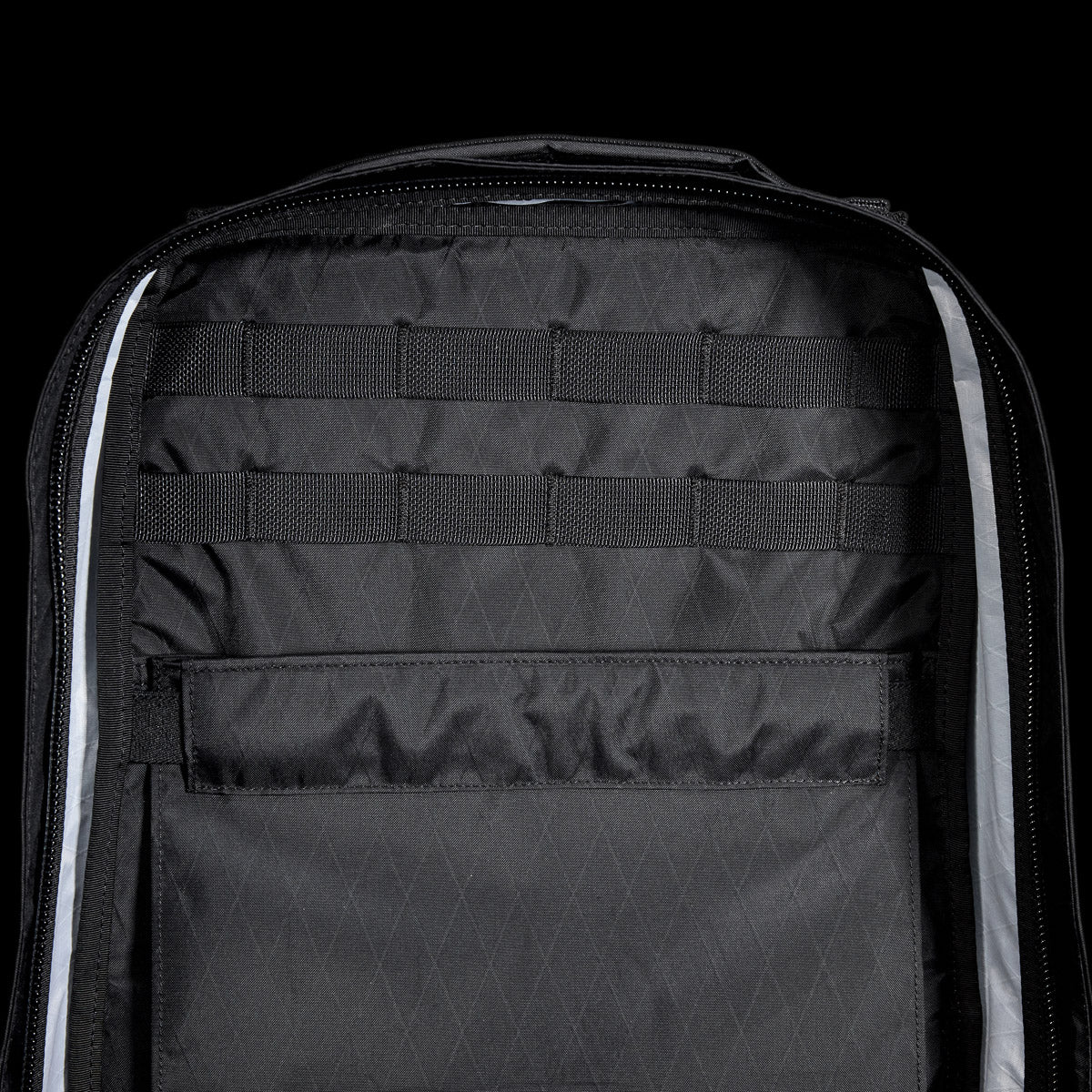 Open black backpack with interior pockets and horizontal webbing straps against a black background.