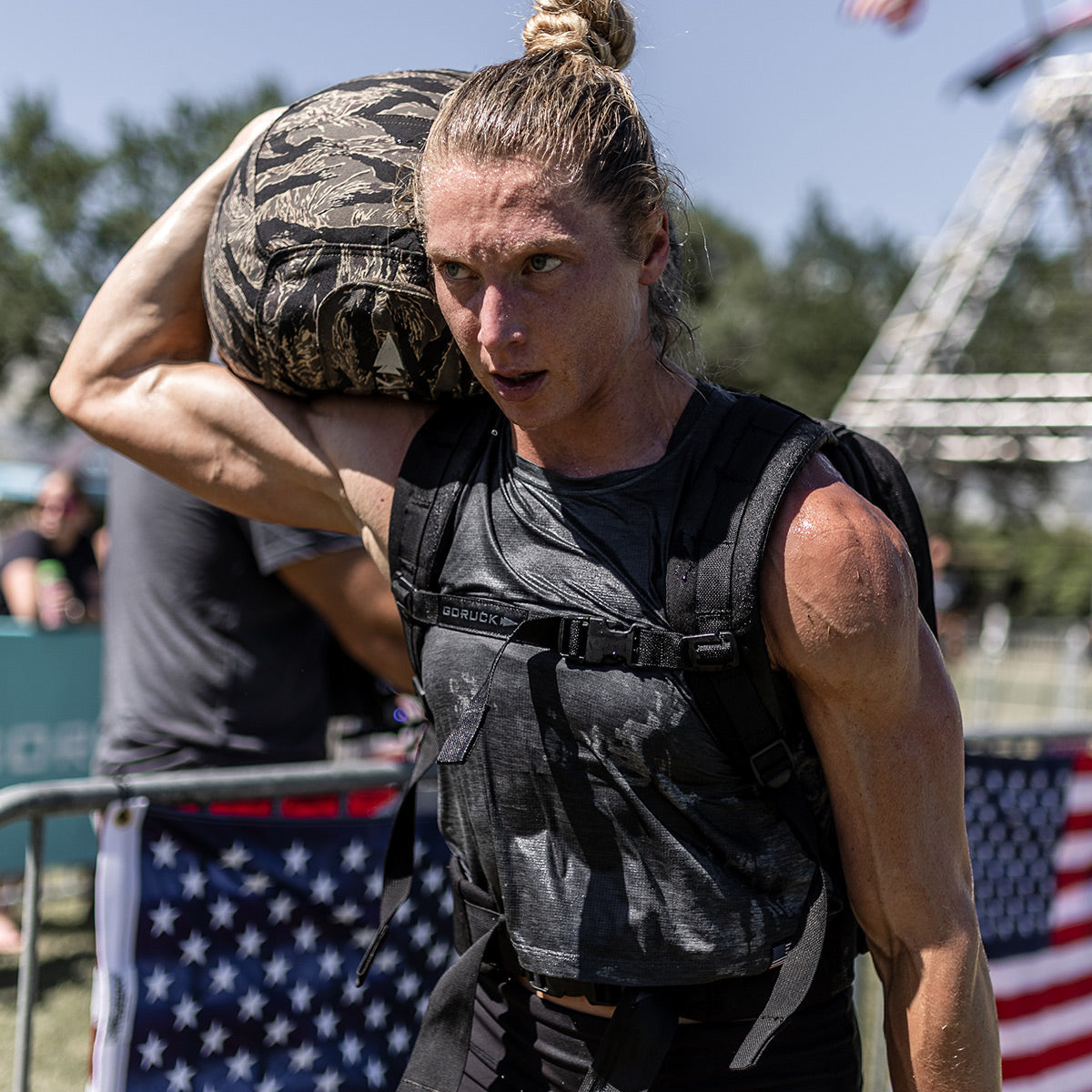 A focused athlete carries a heavy sandbag on their shoulder during an outdoor fitness competition.