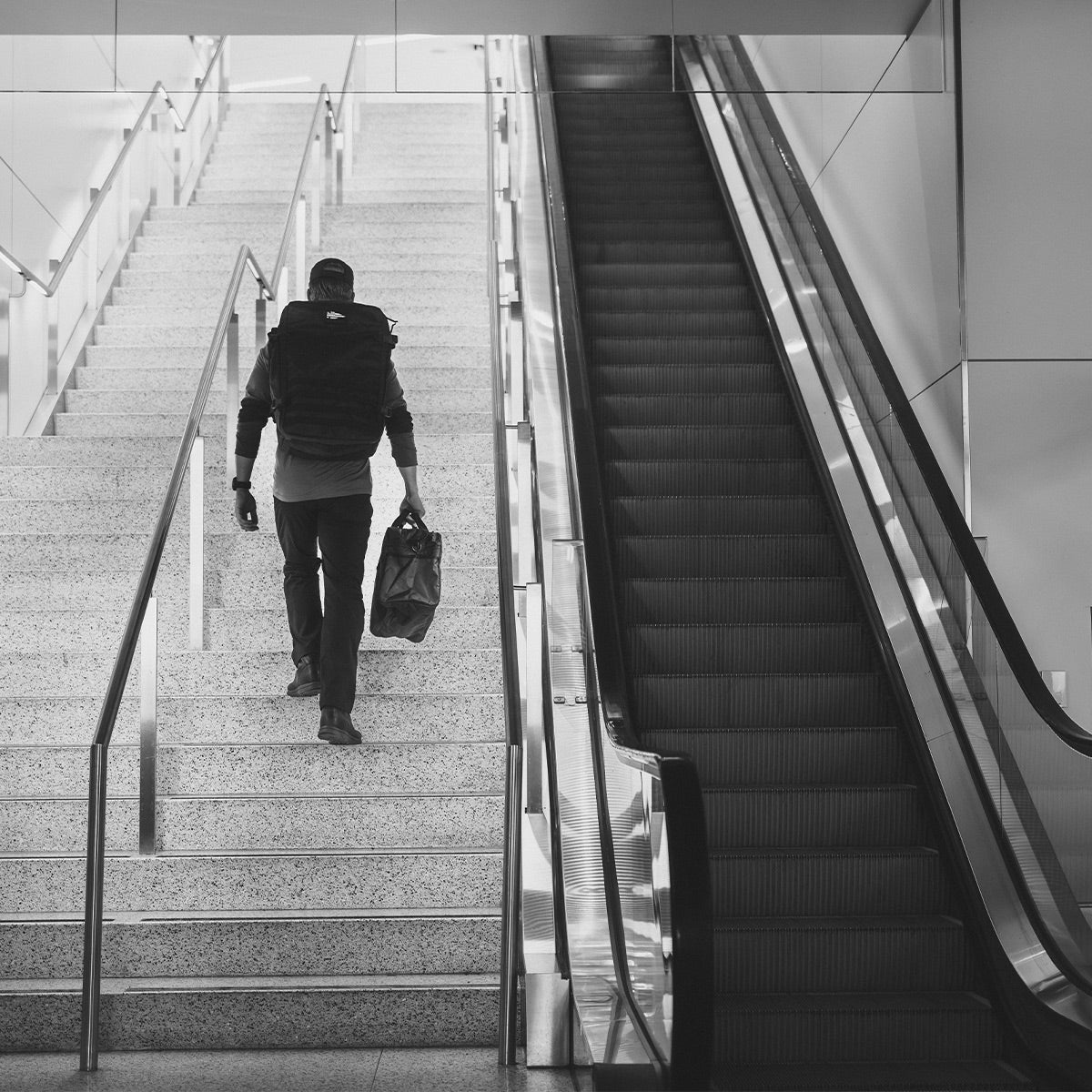 Man carrying a bag walks up stairs beside an empty escalator in a modern building.