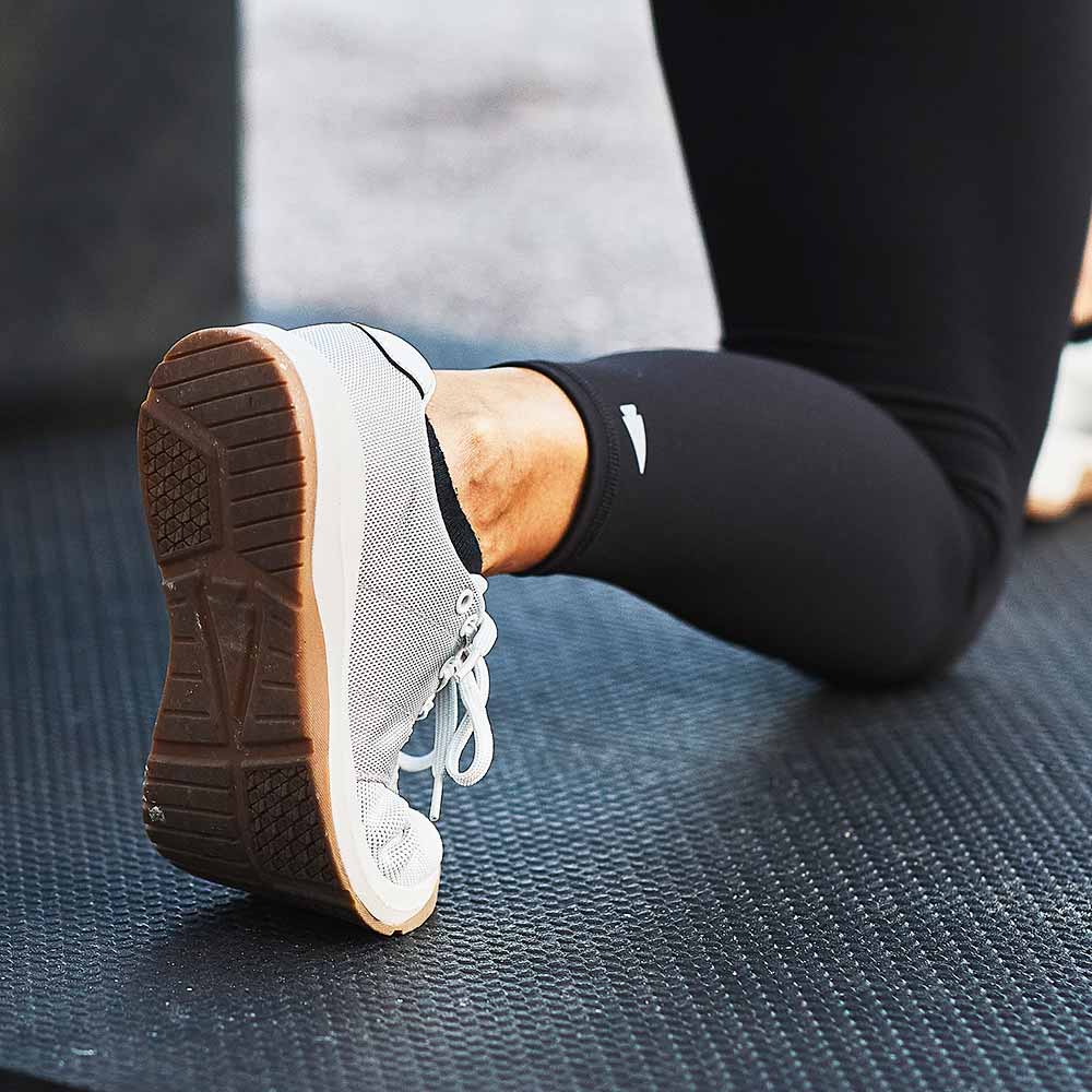 Close-up of a person in athletic shoes and black leggings kneeling on a textured black exercise mat.