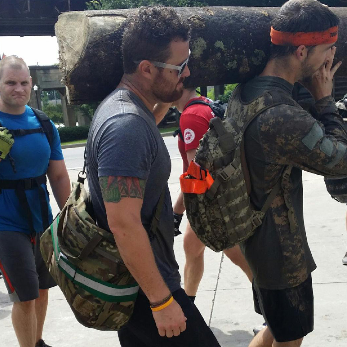 Four men carry a large log on their shoulders during an outdoor endurance event.
