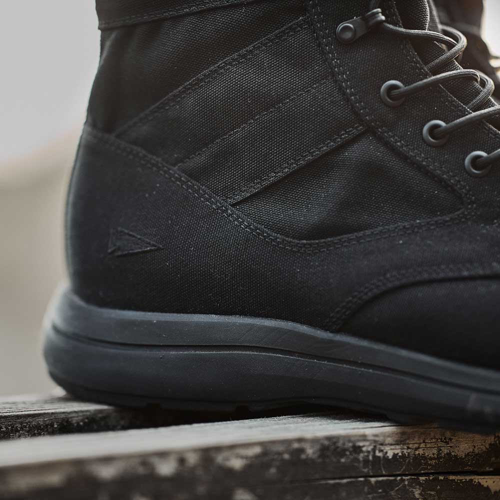 Close-up of a black tactical boot with visible stitching and laces, resting on a wooden surface.