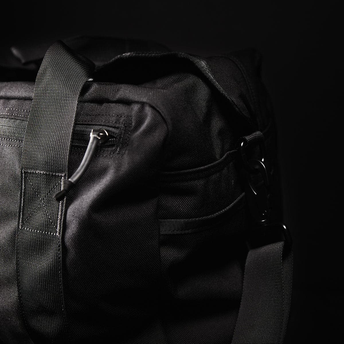 Close-up of a black duffel bag with sturdy straps and a zipper, set against a dark background.