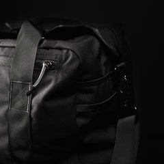 Close-up of a black duffel bag with sturdy straps and a zipper, set against a dark background.