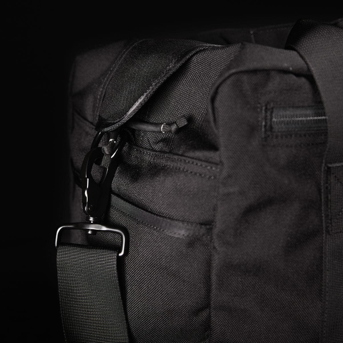 Close-up of a black fabric bag with a strap and metal clasp against a dark background.