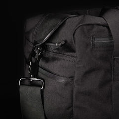 Close-up of a black fabric bag with a strap and metal clasp against a dark background.