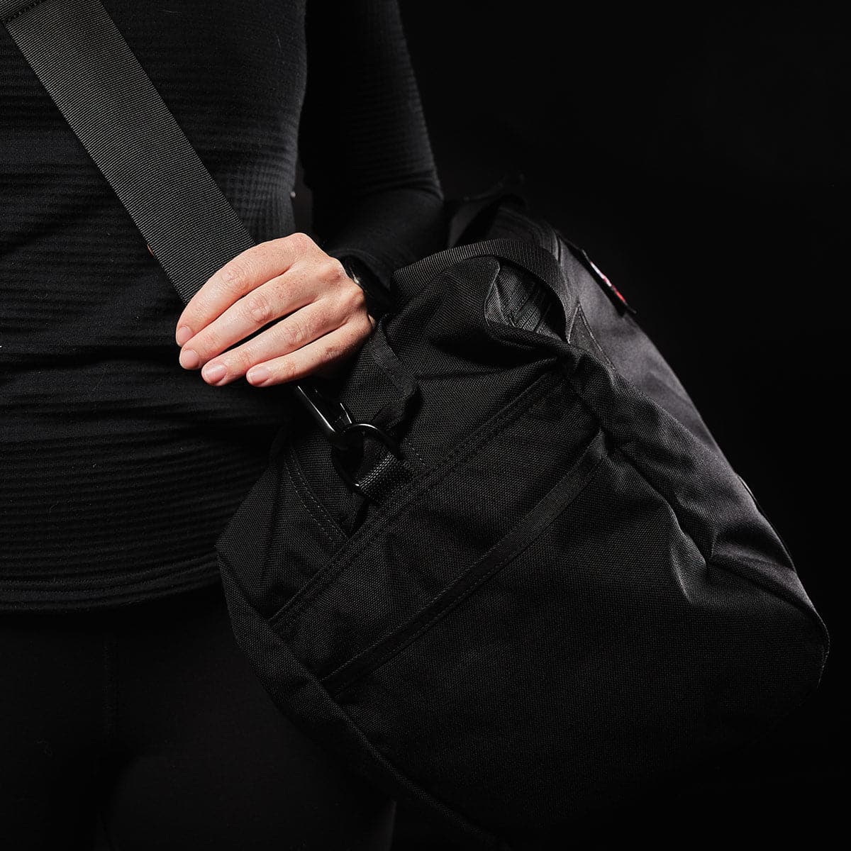 Person carrying GORUCK black rucking gear bag with wide shoulder strap, close-up view
