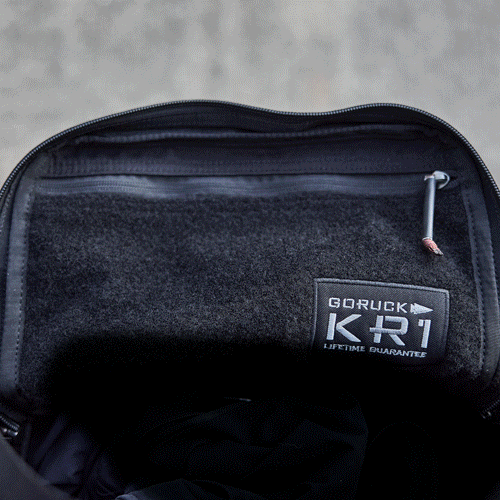 A hand opens a black GORUCK KR1 backpack, showing its interior and the brand label inside.