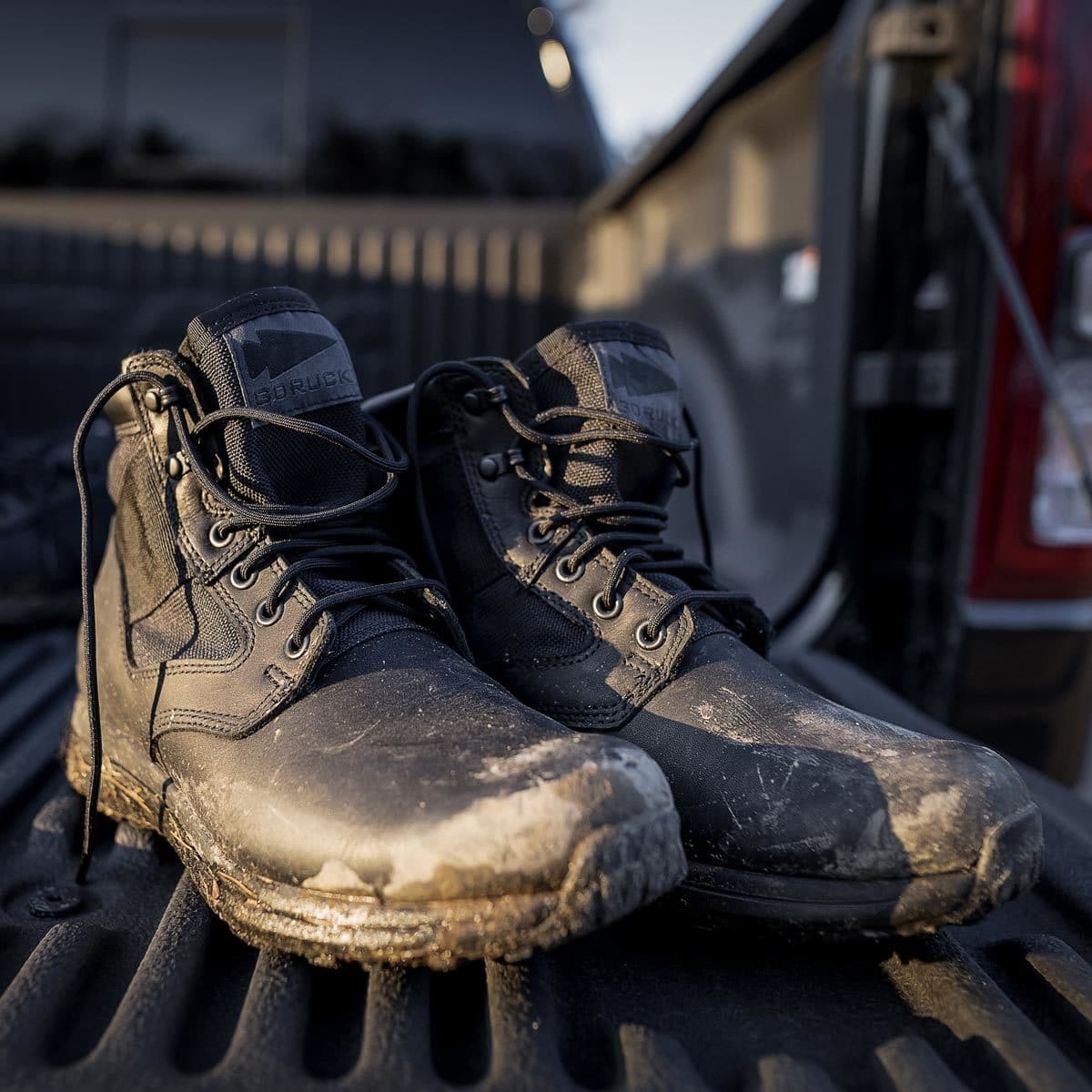 A pair of muddy black boots on the bed of a pickup truck in sunlight.