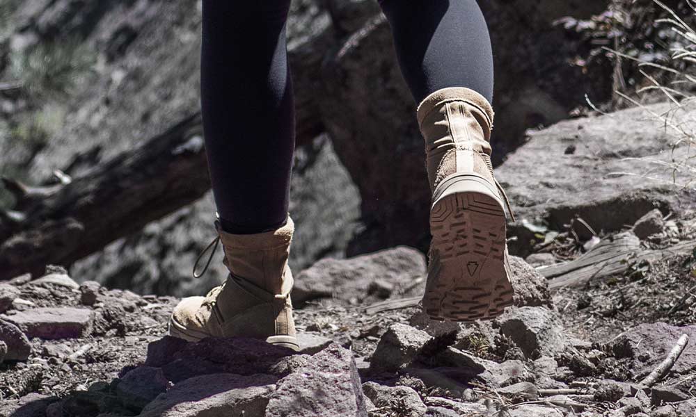 Close-up of a person wearing boots and leggings hiking on a rocky trail outdoors.