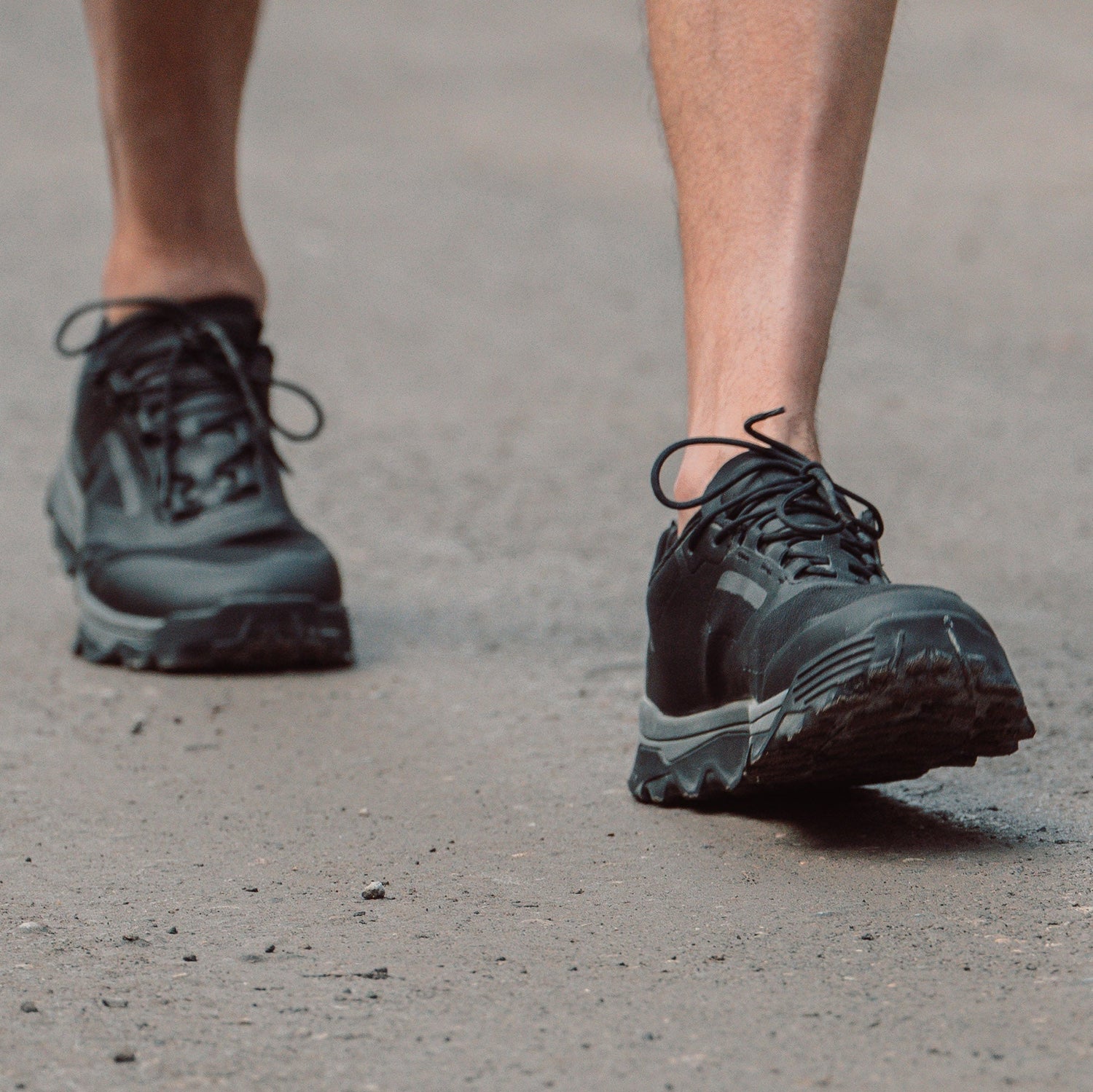 Close-up of a person walking on a paved surface wearing black athletic shoes.