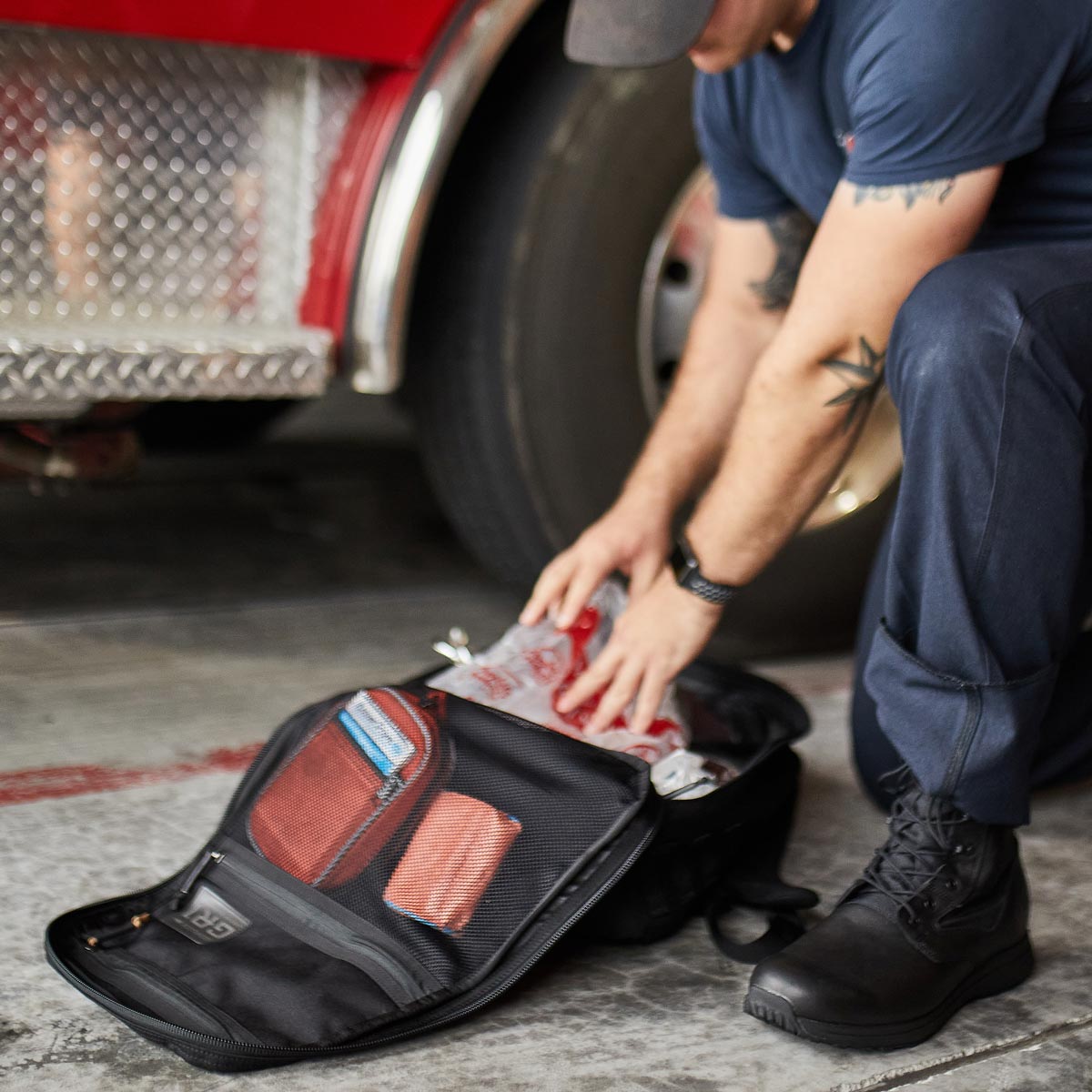 A person packs supplies into an open black bag next to a fire truck.