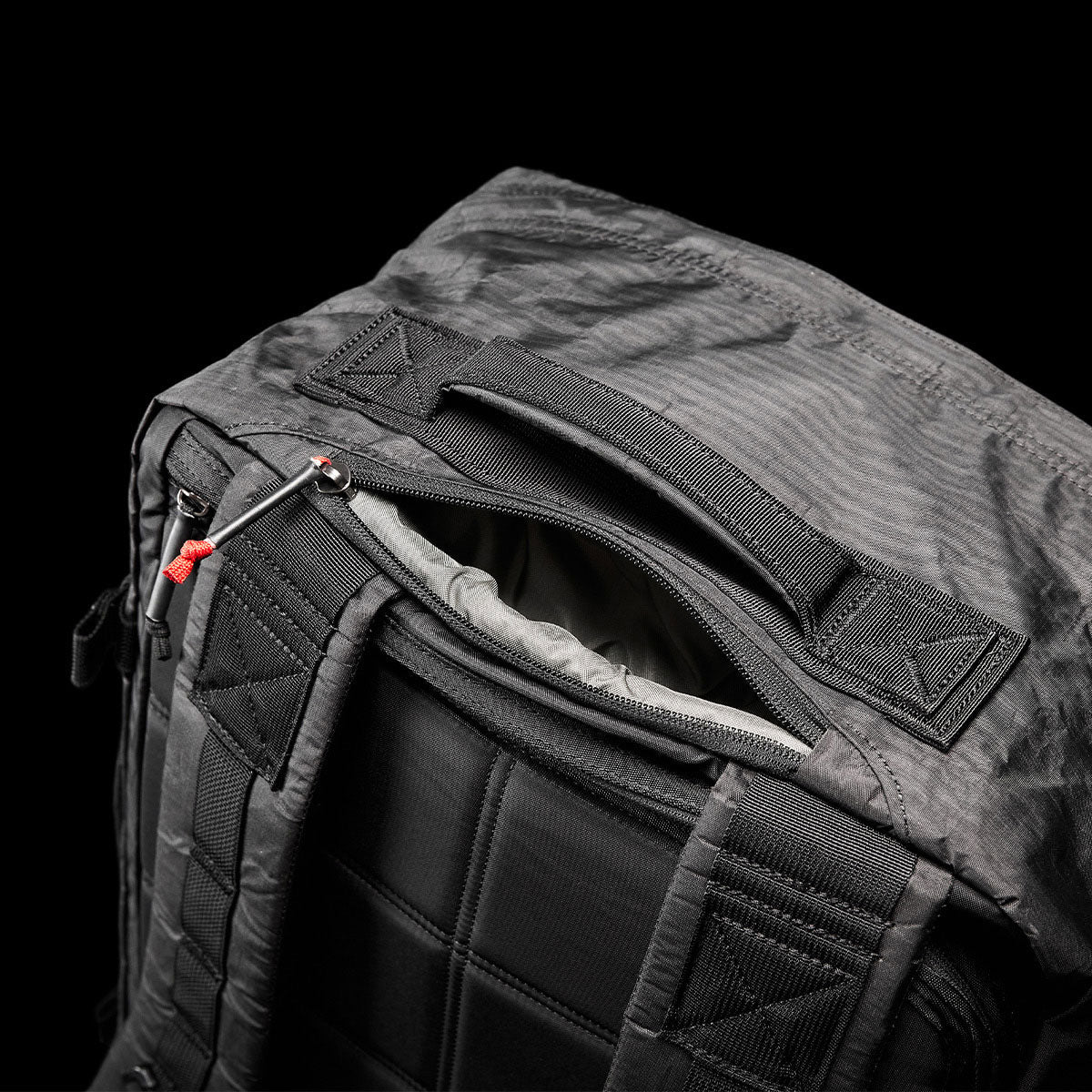 Black backpack with padded straps and an open top pocket, shown against a black background.