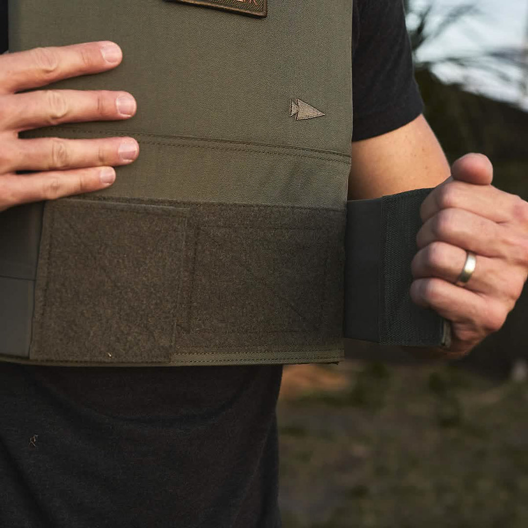 Adjusting the straps of a GORUCK Training Weight Vest 2.0 outdoors, ensuring it's snug for optimal movement.