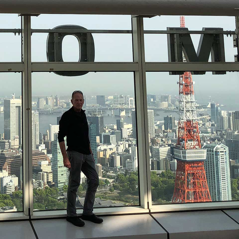 A man stands by windows overlooking Tokyo Tower and city buildings on a sunny day.