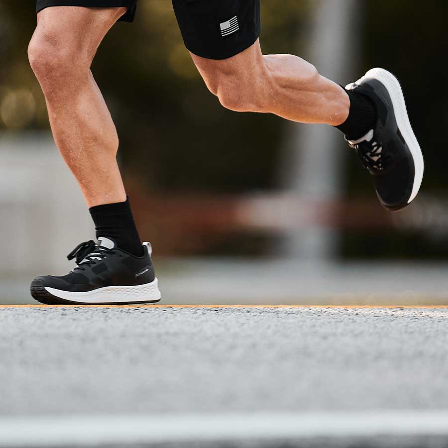 A person running outdoors, wearing black athletic shoes, black socks, and black shorts.