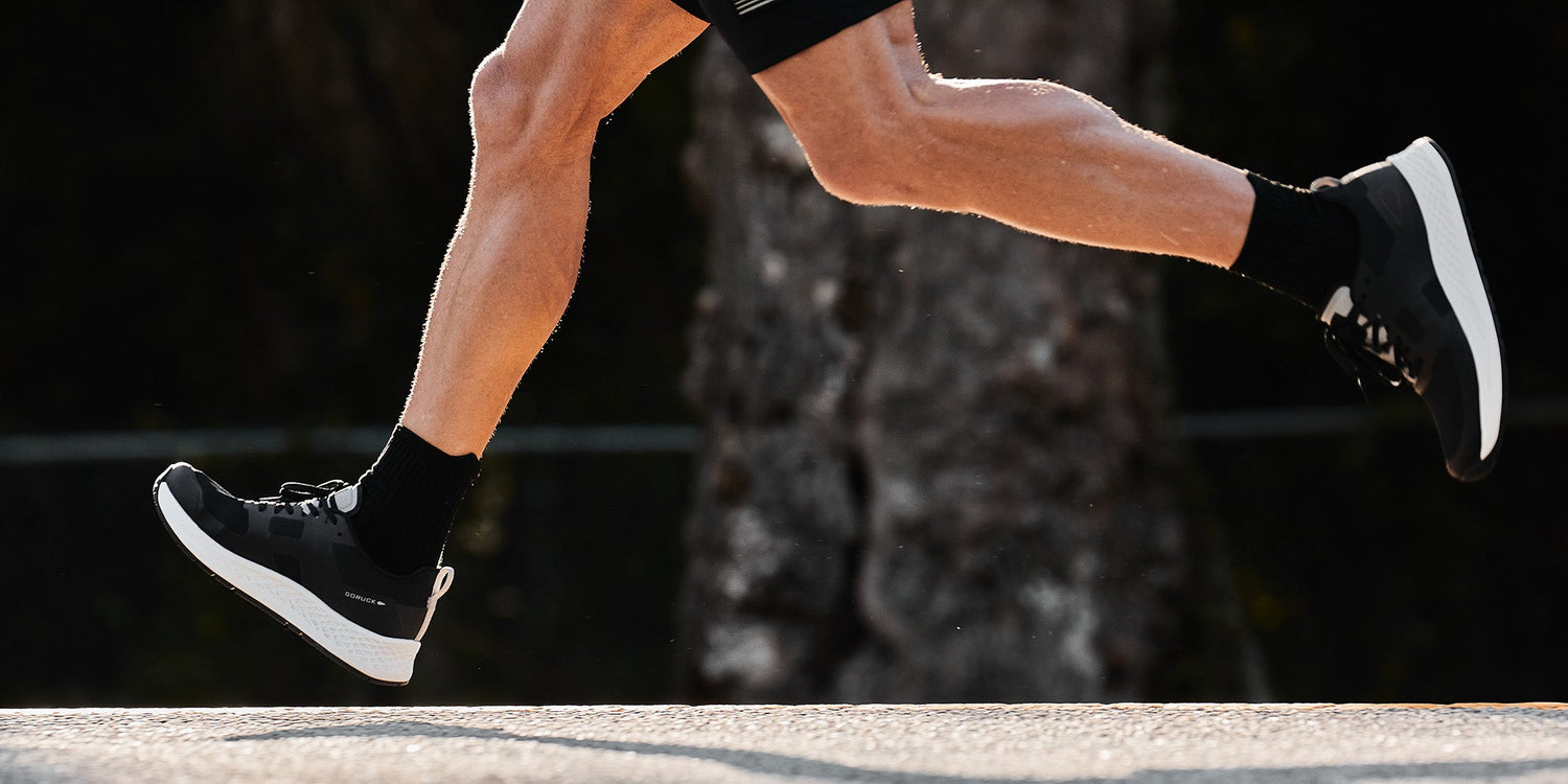 Close-up of a person running outdoors, showing legs in motion and wearing black athletic shoes and socks.