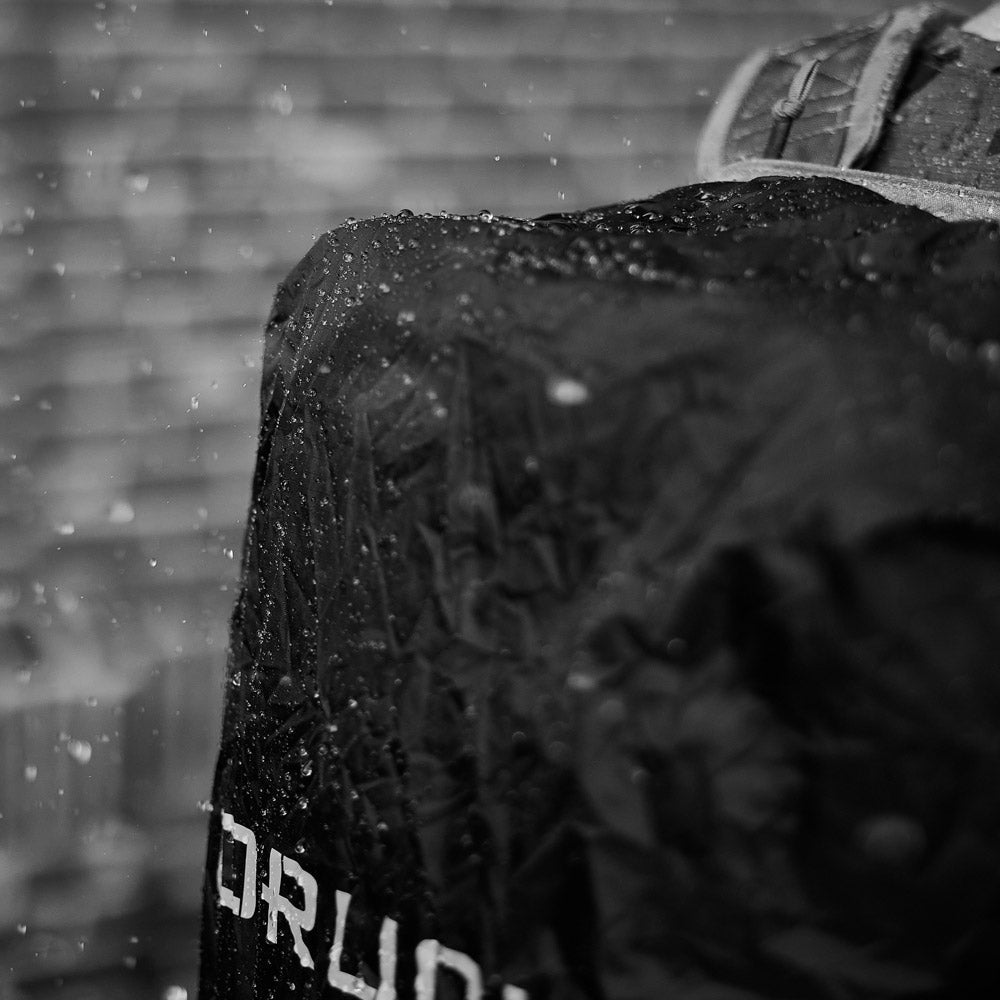 A wet backpack in the rain with water droplets and blurred brick wall in the background.