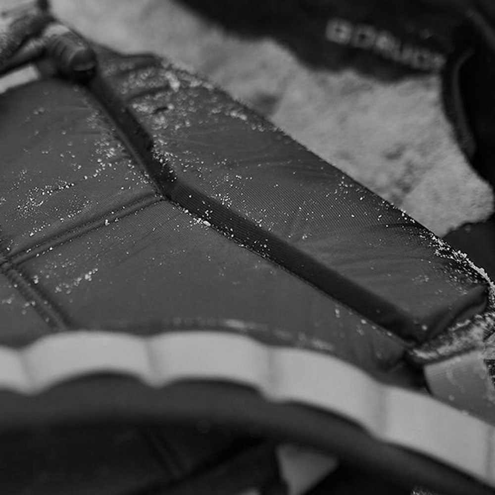 Close-up of a padded black backpack with sand scattered on its surface.