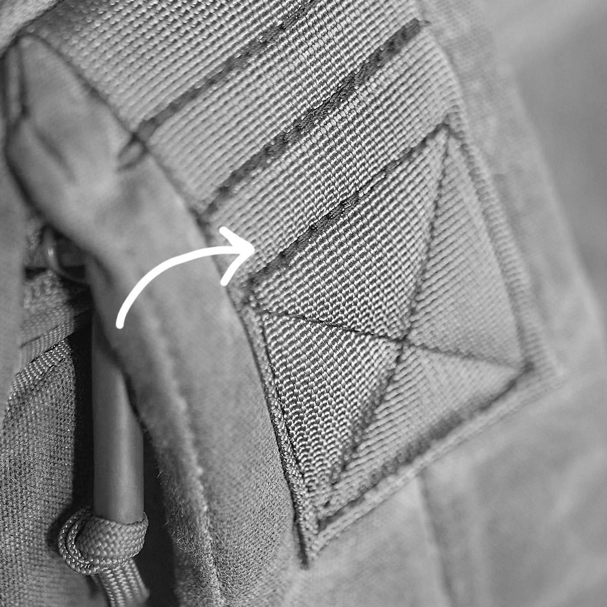 Close-up of a fabric strap with reinforced stitching and an arrow pointing to it.