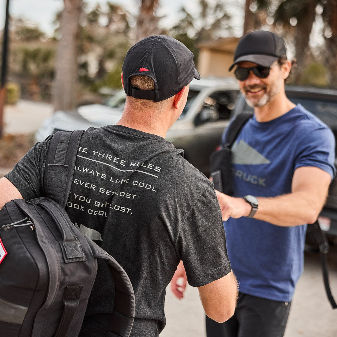 Two men in athletic gear greet each other outside; one is wearing a GORUCK Performance Running Hat - ToughMesh.