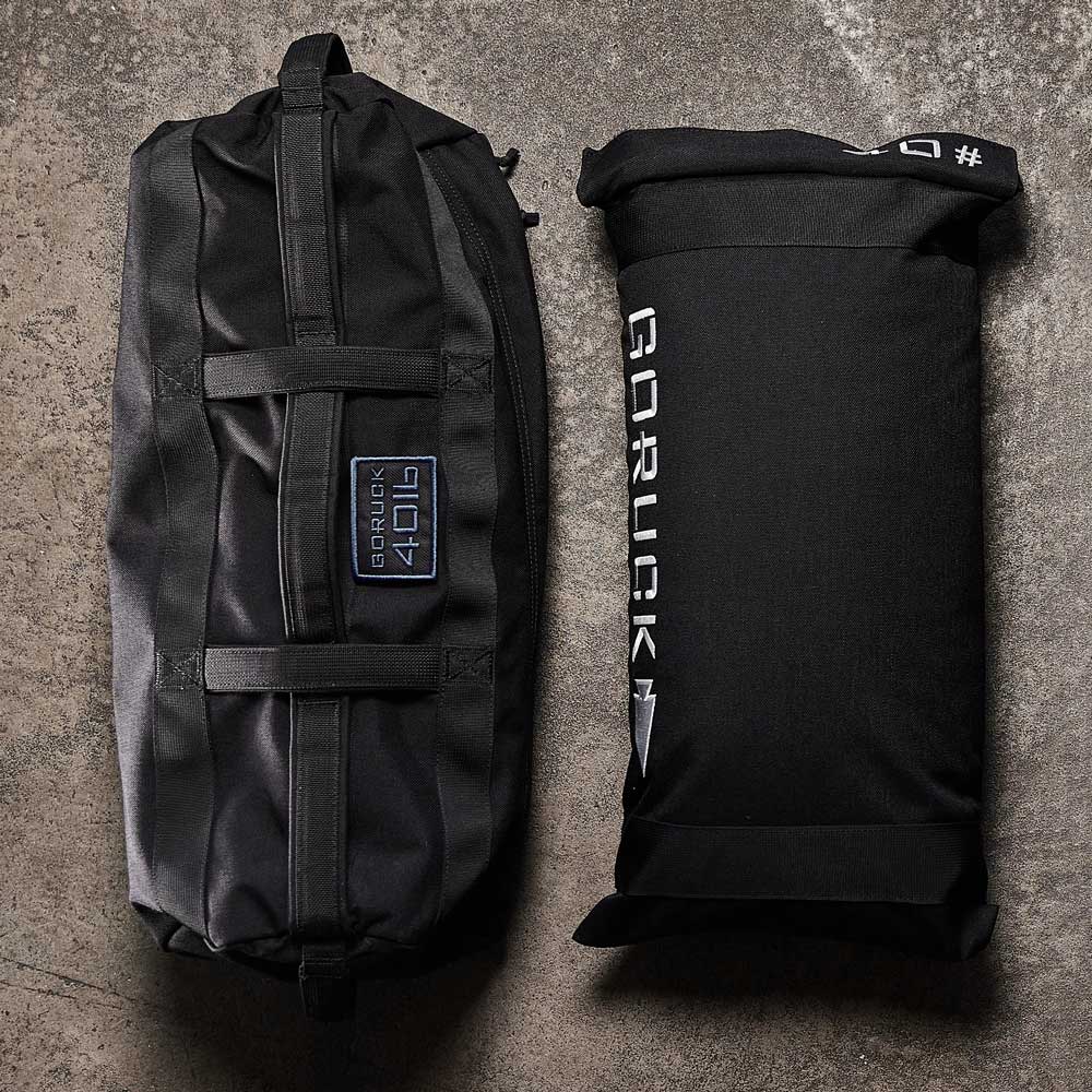 Two black GORUCK gym bags on a concrete floor, one cylindrical and one rectangular.